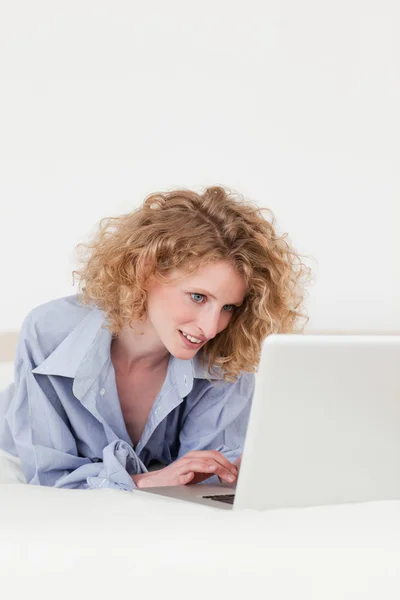 Ładny blond kobieta relaksując się przy jej laptop leżąc na jej — Zdjęcie stockowe
