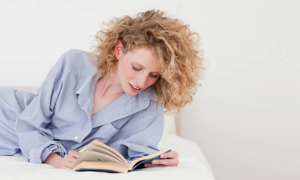 美丽的金发女人躺在她的床上时读一本书 — 图库照片