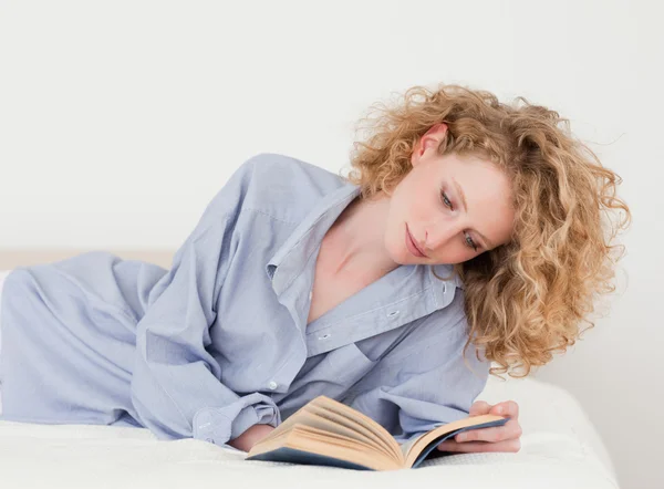 Beautiful blonde woman reading a book while lying on her bed — Stock Photo, Image