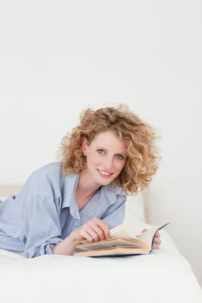 Attractive blonde woman reading a book while lying on her bed — Stock Photo, Image