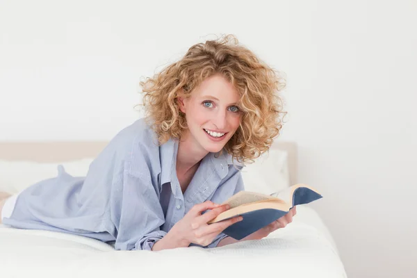 Dobře vypadající blondýnka čtení knihy vleže na posteli — Stock fotografie