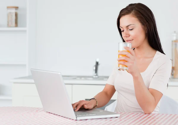 Brunette using her laptop and drinking orange juice — Stock Photo, Image