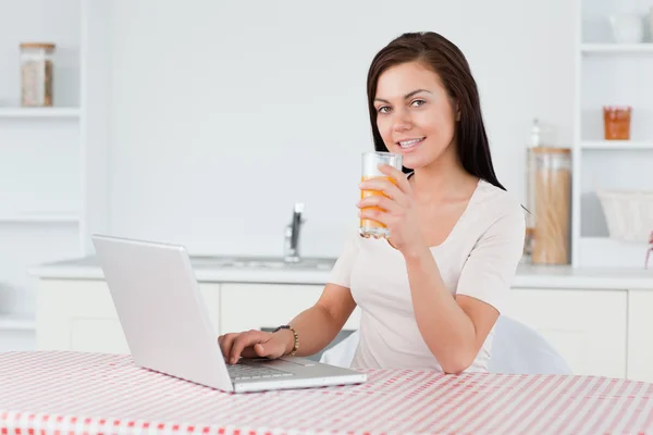 Young woman using her laptop and drinking orange juice — Stock Photo, Image