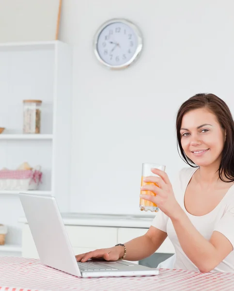 Portrait of a brunette using her laptop and drinking juice — Stock Photo, Image