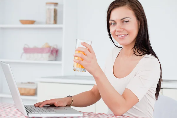 Close up of a brunette using her laptop and drinking juice — Stock Photo, Image