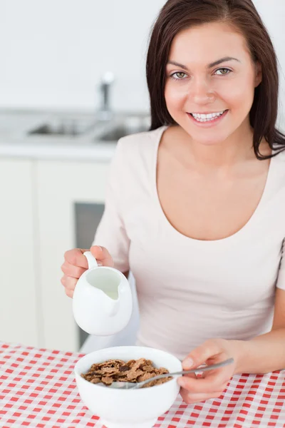 Porträtt av en brunett hälla mjölk i hennes spannmål — Stockfoto