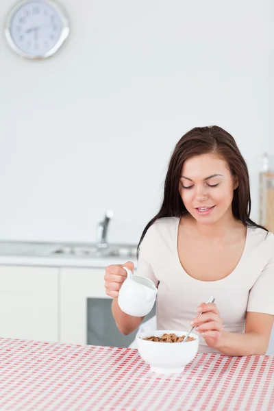 Retrato de una mujer sonriente echando leche en su cereal — Foto de Stock