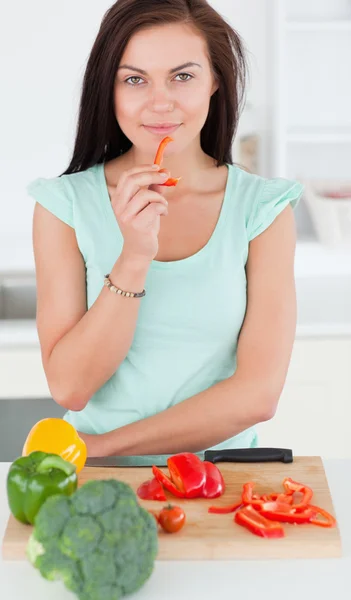 Porträt einer charmanten Frau, die eine Scheibe Paprika isst — Stockfoto