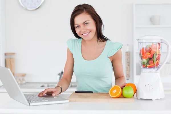 Morena bonito com um laptop e frutas — Fotografia de Stock