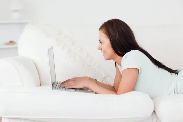 Χαριτωμένο γυναίκα σε ένα καναπέ, χρησιμοποιώντας ένα φορητό υπολογιστή — Φωτογραφία Αρχείου