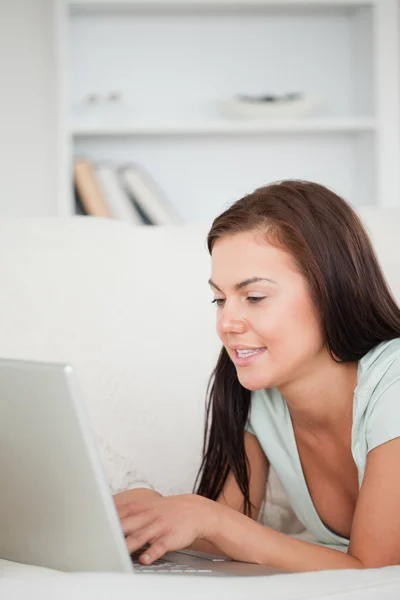 Portrait of a cute brunette on a sofa using a laptop — Stock Photo, Image