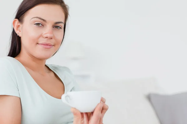 Close up de uma mulher encantadora sentada em um sofá com uma xícara de chá — Fotografia de Stock