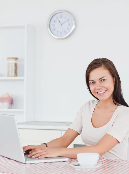 Morena sorridente usando seu laptop e tomando um chá — Fotografia de Stock