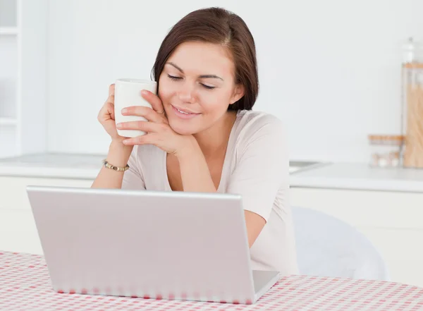 Χαριτωμένο μελαχρινός γυναίκα χρησιμοποιώντας το laptop της και έχοντας ένα τσάι — Φωτογραφία Αρχείου