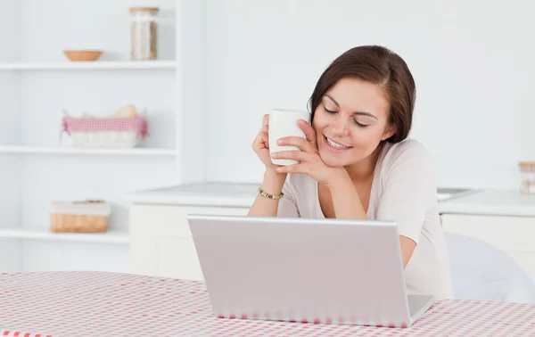 Aranyos barna lány laptop használ és birtoklás egy tea — Stock Fotó