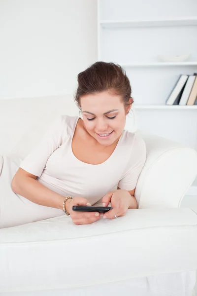 Linda morena mensajes de texto mientras está acostada en su sofá —  Fotos de Stock