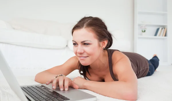 Jeune femme couchée sur un tapis avec un ordinateur portable — Photo