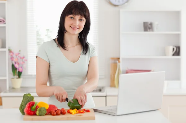 Leende brunett kvinna matlagning medan du kopplar av med sin laptop — Stockfoto