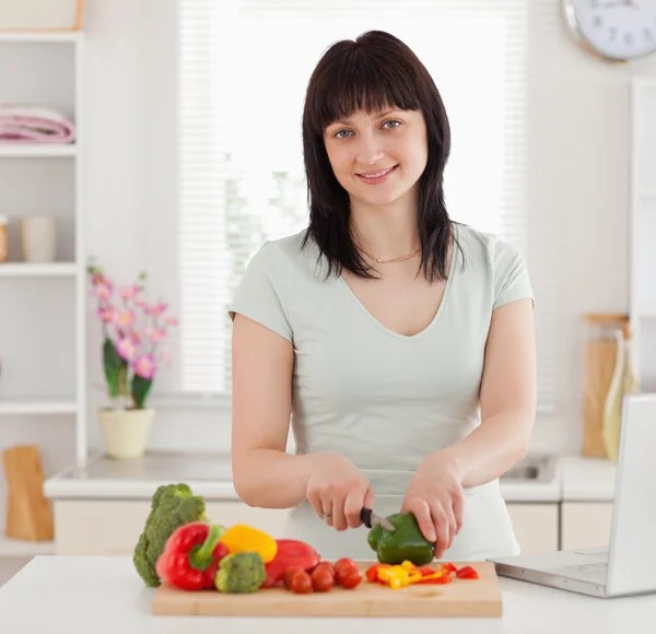 Söt brunett kvinna matlagning medan du kopplar av med sin laptop — Stockfoto