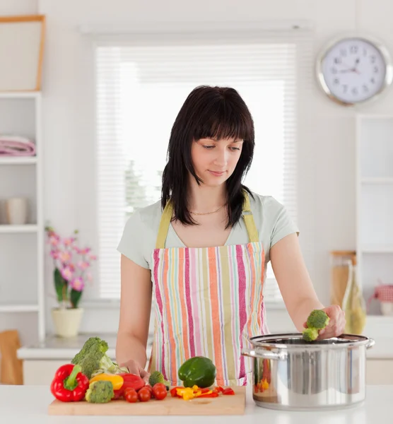 Jolie femme brune posant tout en cuisinant des légumes — Photo