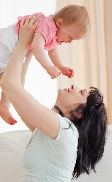 Niedliche Frau hält ihr Baby auf dem Arm, während sie auf einem Sofa sitzt — Stockfoto