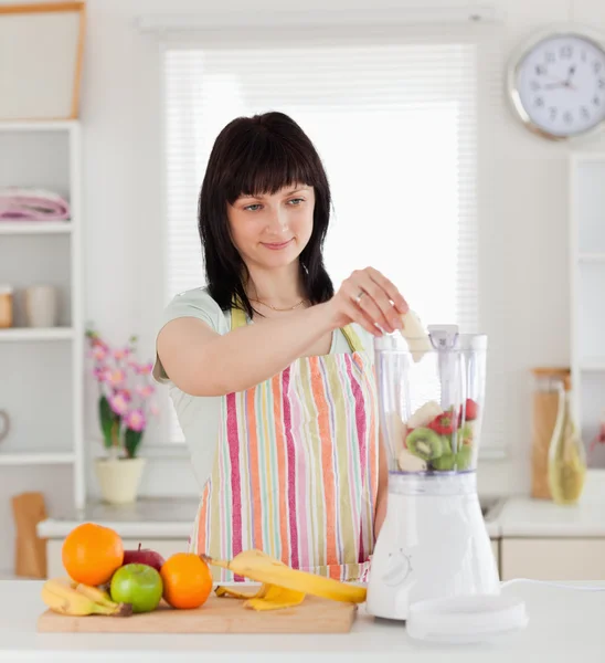 Attraktive brünette Frau legt Gemüse in einen Mixer, während st — Stockfoto