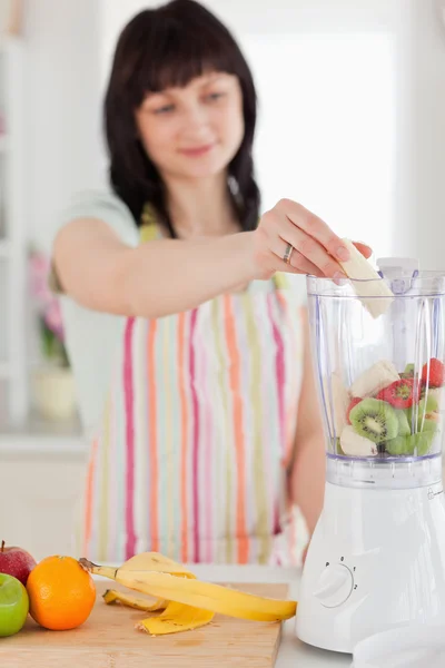 Charmante brünette Frau legt Gemüse in einen Mixer, während stan — Stockfoto