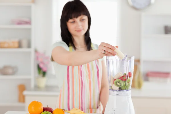 Bella donna bruna che mette le verdure in un mixer mentre standi — Foto Stock
