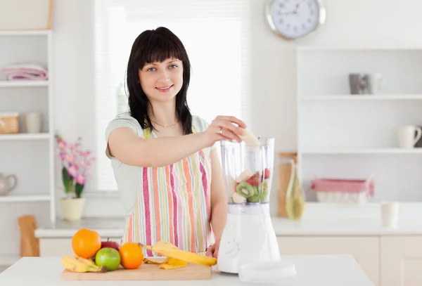 Femme brune mignonne mettant des légumes dans un mélangeur tout en se tenant debout — Photo