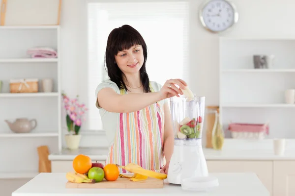 Wunderschöne brünette Frau legt Gemüse in einen Mixer, während stan — Stockfoto