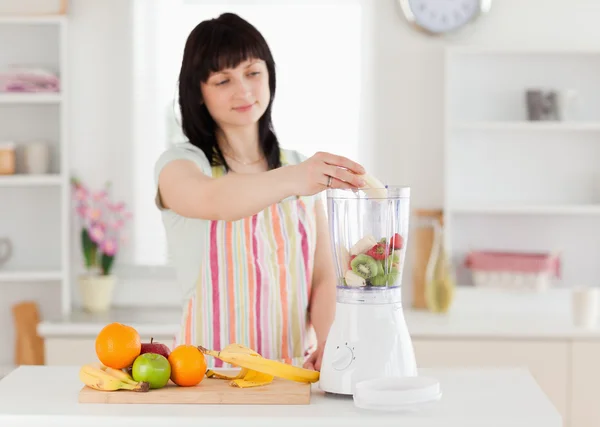 Schöne brünette Frau legt Gemüse in einen Mixer, während Standi — Stockfoto