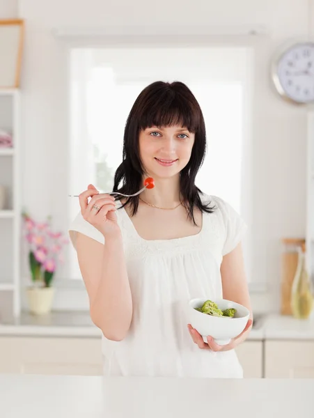 Cute brunette female eating a cherry tomato while holding a bowl — Stock Photo, Image