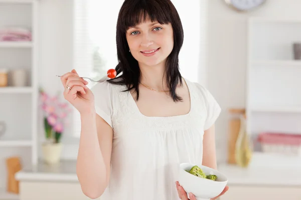 Attraktive brünette Frau isst eine Kirschtomate, während sie hält — Stockfoto