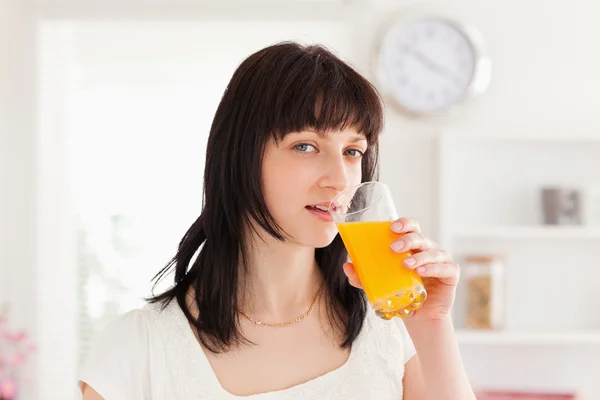 Ładna brunetka picia szklankę soku pomarańczowego, stojąc — Zdjęcie stockowe