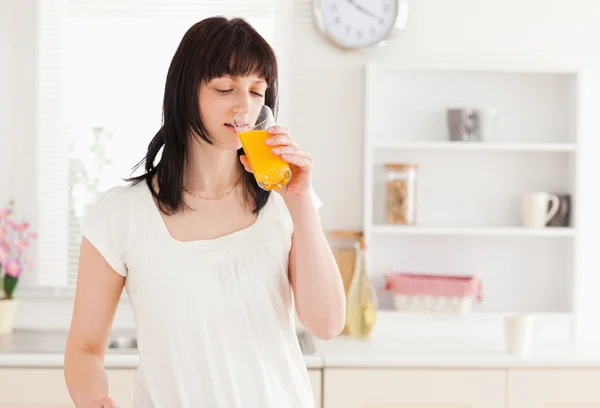 Piękne brunetki picia szklankę soku pomarańczowego, stojąc — Zdjęcie stockowe