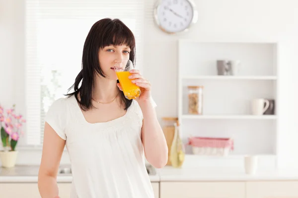 Hermosa morena bebiendo un vaso de jugo de naranja mientras está de pie — Foto de Stock