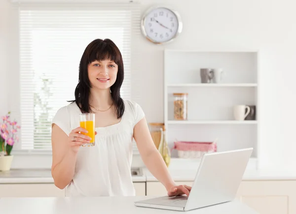 Attraktiv brunett kvinna håller ett glas apelsinjuice medan — Stockfoto