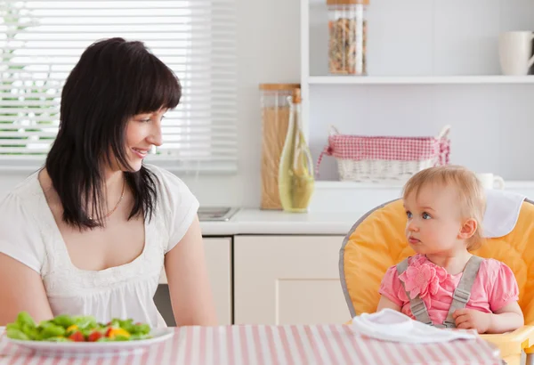Hermosa mujer morena comiendo con su bebé mientras está sentada —  Fotos de Stock