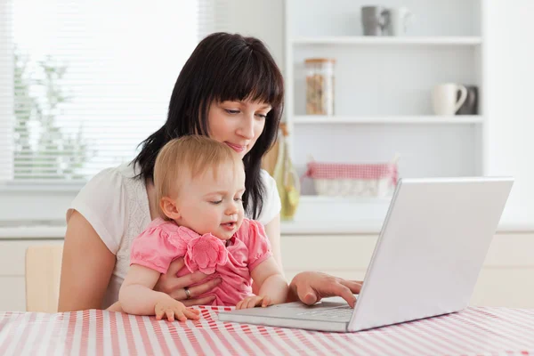 Attrayant brunette femme montrant son ordinateur portable à son bébé tandis que s — Photo