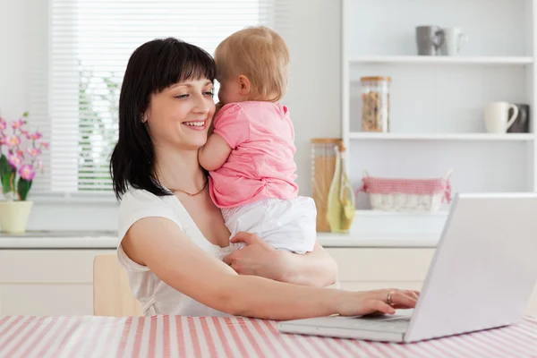 Гарненька брюнетка жінка розслабляється зі своїм ноутбуком поруч зі своєю дитиною — стокове фото