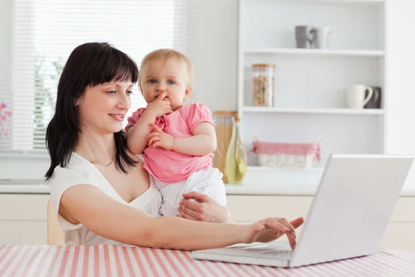 Мила брюнетка жінка розслабляється зі своїм ноутбуком поруч зі своєю дитиною — стокове фото