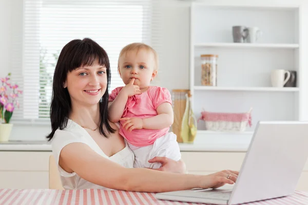 Όμορφη μελαχρινή γυναίκα, χαλαρωτικό με το laptop δίπλα το μωρό — Φωτογραφία Αρχείου