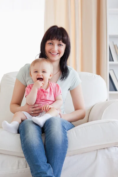 Atrakcyjna kobieta trzyma swoje dziecko w ramiona siedząc — Zdjęcie stockowe