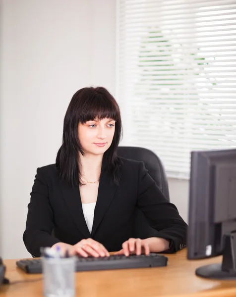 Atractiva mujer morena trabajando en una computadora mientras está sentada en —  Fotos de Stock