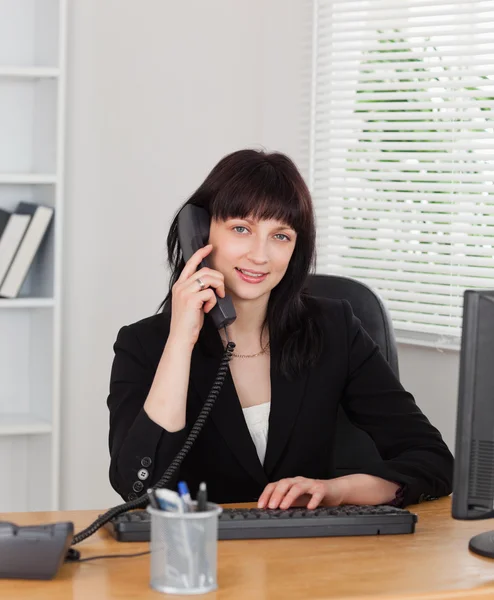 Gut aussehende brünette Frau am Telefon, während sie an einem Comp arbeitet — Stockfoto
