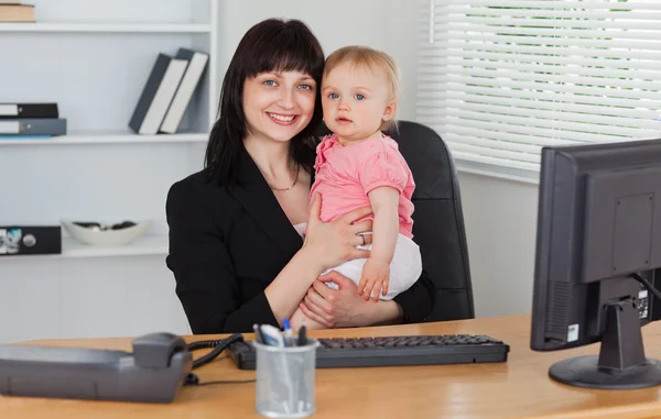 Gut aussehende brünette Frau posiert, während sie ihr Baby auf ihrem Arm hält — Stockfoto