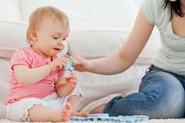 Female showing a puzzle piece to her baby while sitting on a car — Stock Photo, Image