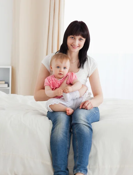 Schöne brünette Frau hält ihr Baby auf den Knien, während sie sitzt — Stockfoto