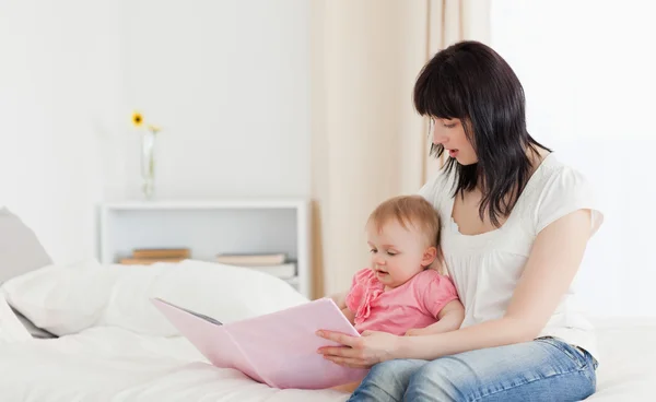 Attraktive brünette Frau zeigt ihrem Baby beim Sitzen ein Buch — Stockfoto