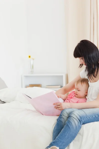 Goede zoek brunette vrouw tonen een boek aan haar baby terwijl sit — Stockfoto